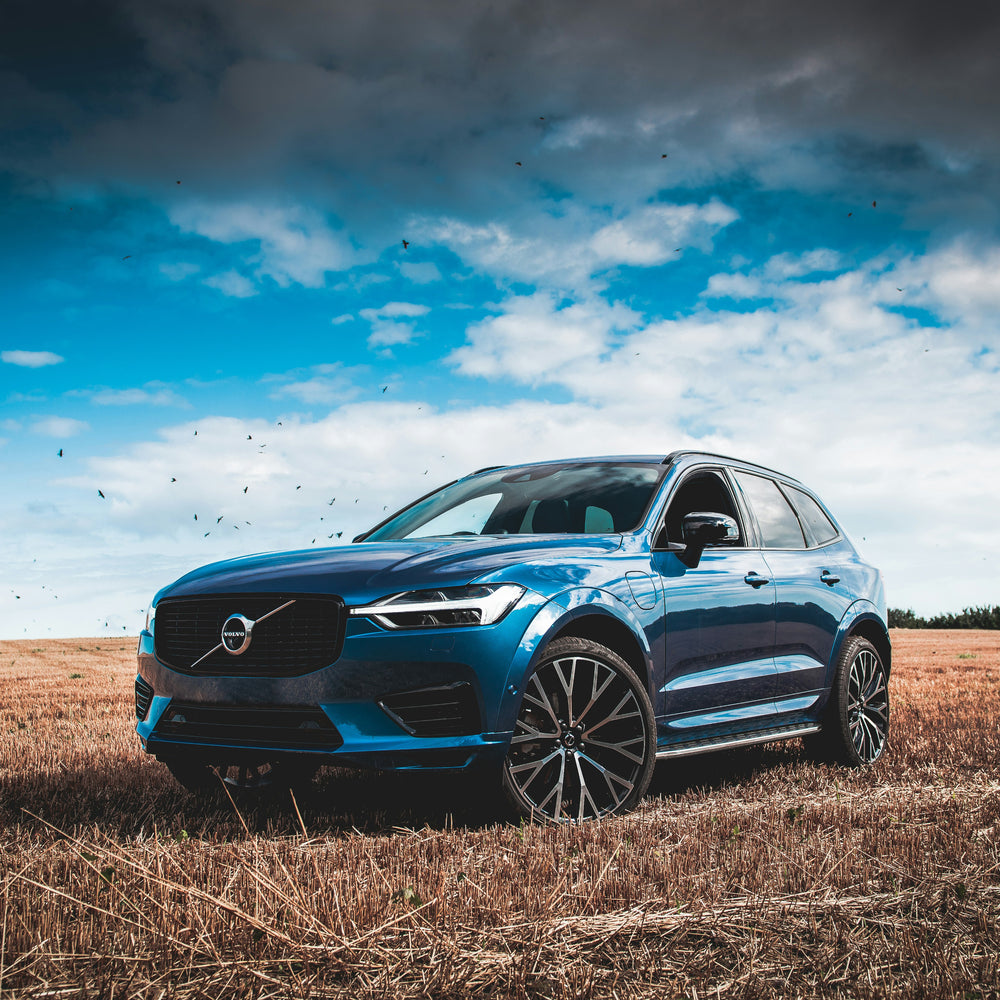Blue Volvo SUV parked in a field with a blue sky and clouds.